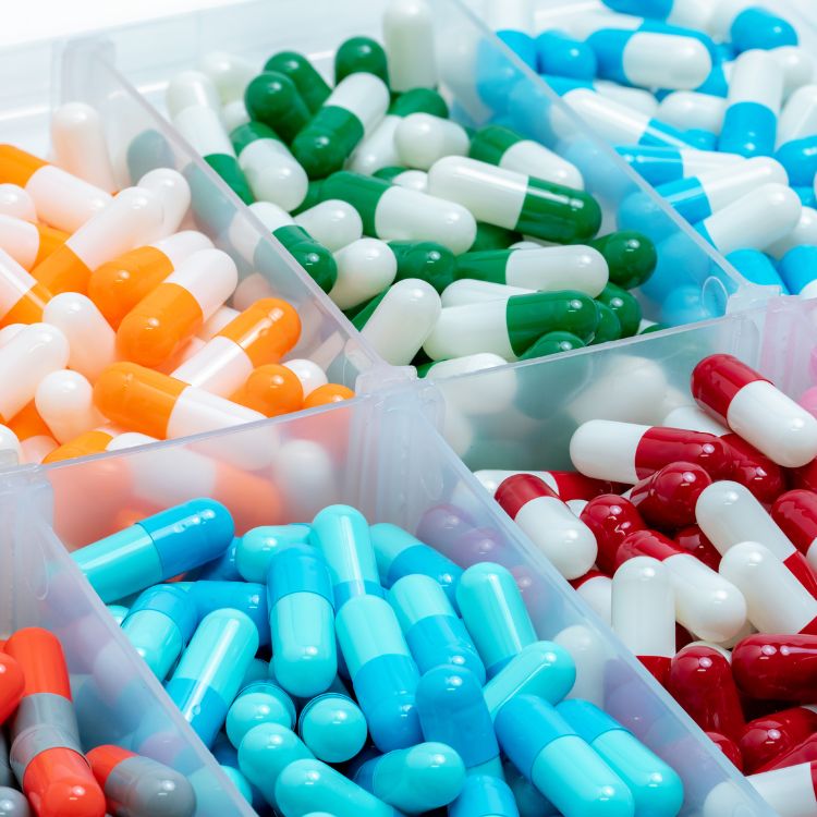 A plastic box with compartments filled with different colored empty capsules.