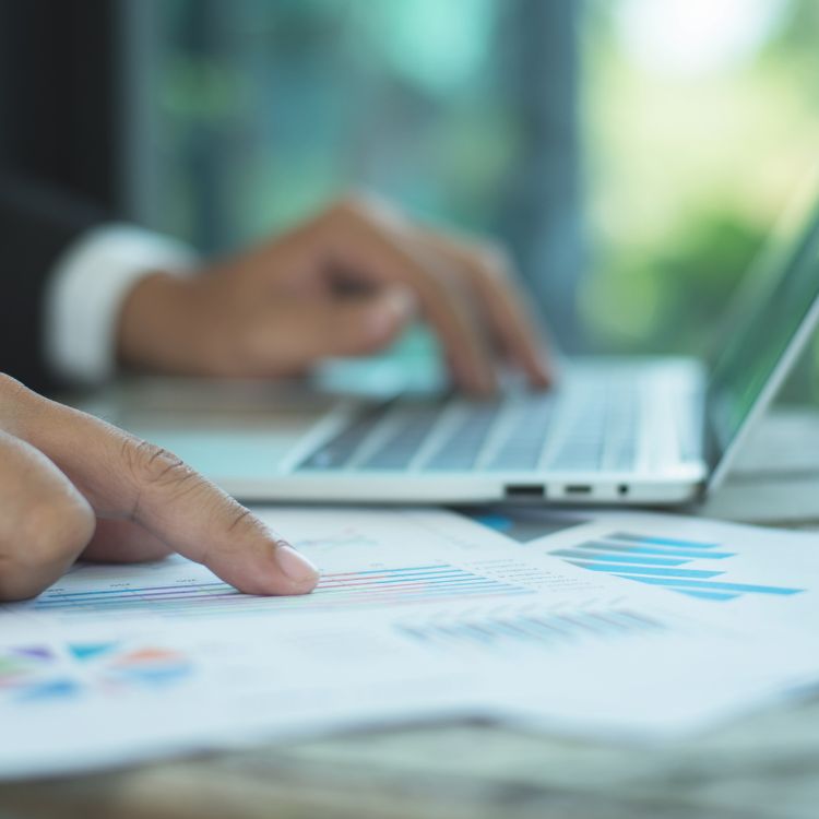 Close up of business professional determining cost considerations with a laptop and graphs on paper.